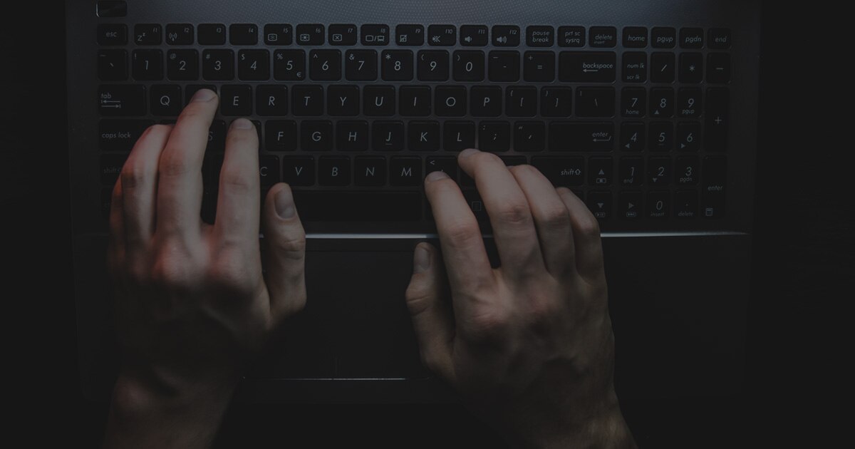 A person typing on a keyboard to access the dark web.